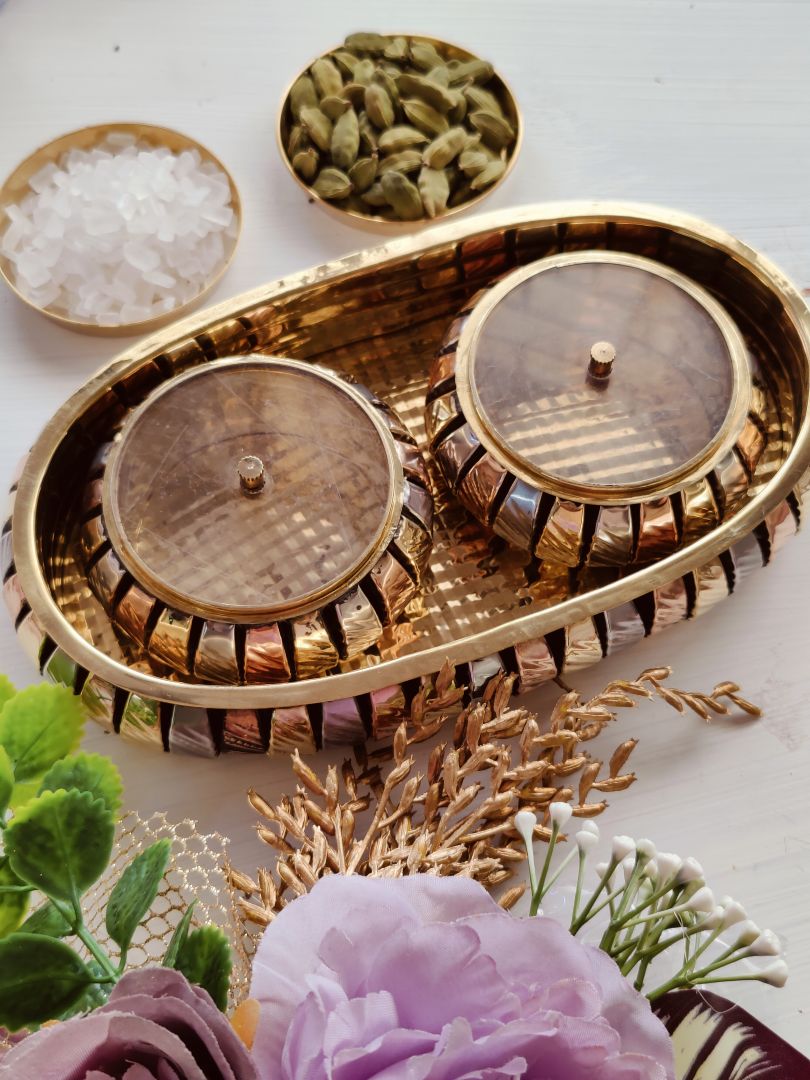 Brass gift box set showing two small brass bowls with condiments on a textured
tray, styled with flowers to highlight the aroma & aura gift box theme.