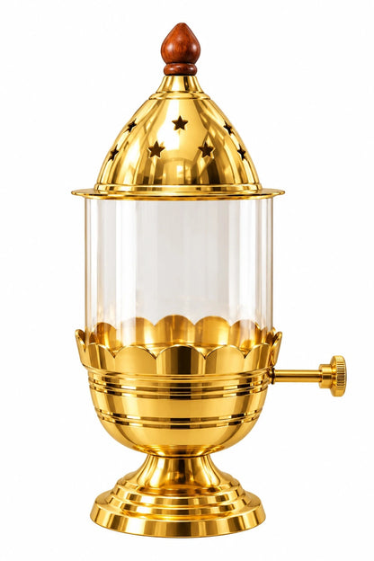 A gold-toned decorative lantern or lamp with a clear glass body, star-cutout dome top, and small side knob, shown on a plain white background. Akand diya 