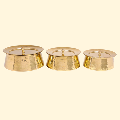 Set of three Bulkysanta hammered brass handis, each with its lid on. The pots are gold-colored and feature a textured, hammered finish.