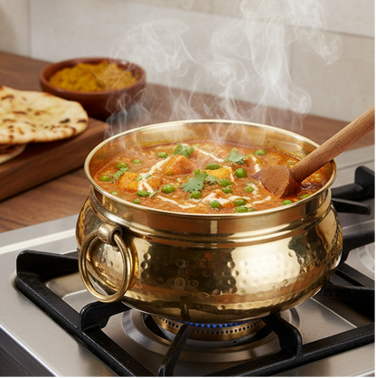 Classic Pot Style Brass Handi, Degchi, Patila (Pital ki handi, Pital ka Patila, Pital ke bartan) used for cooking a tempting Paneer and Pea Curry (Matar Paneer) on a gas stove, with visible steam and a wooden spoon. The pot features a rounded shape and a large brass ring handle. Naan bread and spices are visible in the background.