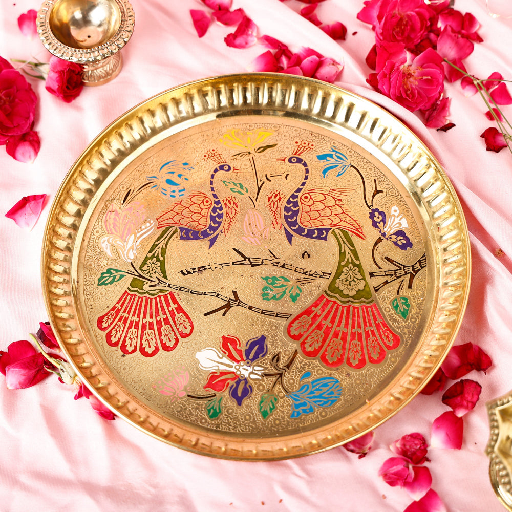 Decorative brass plate with peacock design on a pink fabric background with flowers