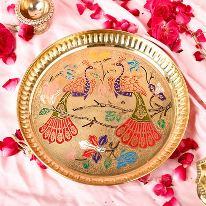 Decorative brass plate with peacock design on a pink fabric background with flowers