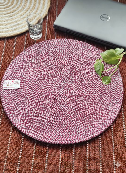 Round woven placemat on a wooden surface with a laptop and glass in the background.
