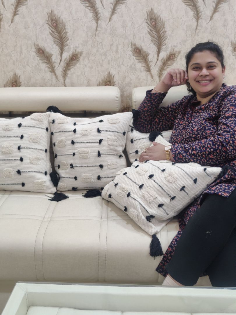 Cream embroidered luxury cushion covers with tassels placed beside a seated person.
