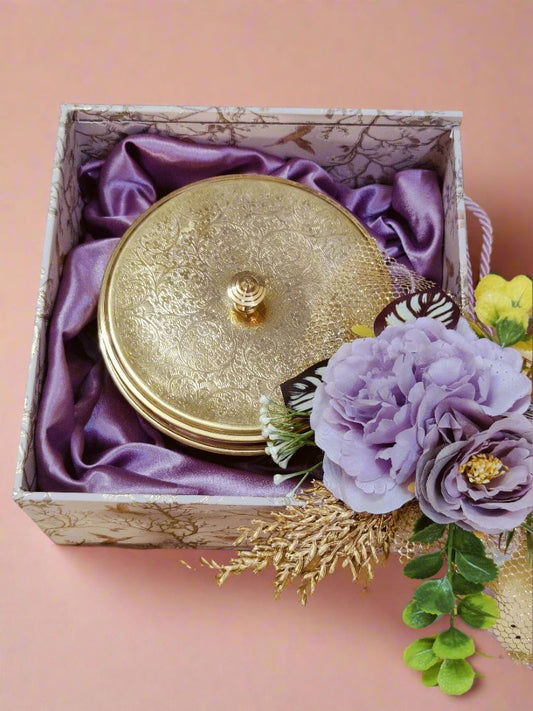 Brass spice box gift set shown with purple flowers and silk lining inside a patterned box, presenting a handcrafted brass masala box gift set for occasions.​