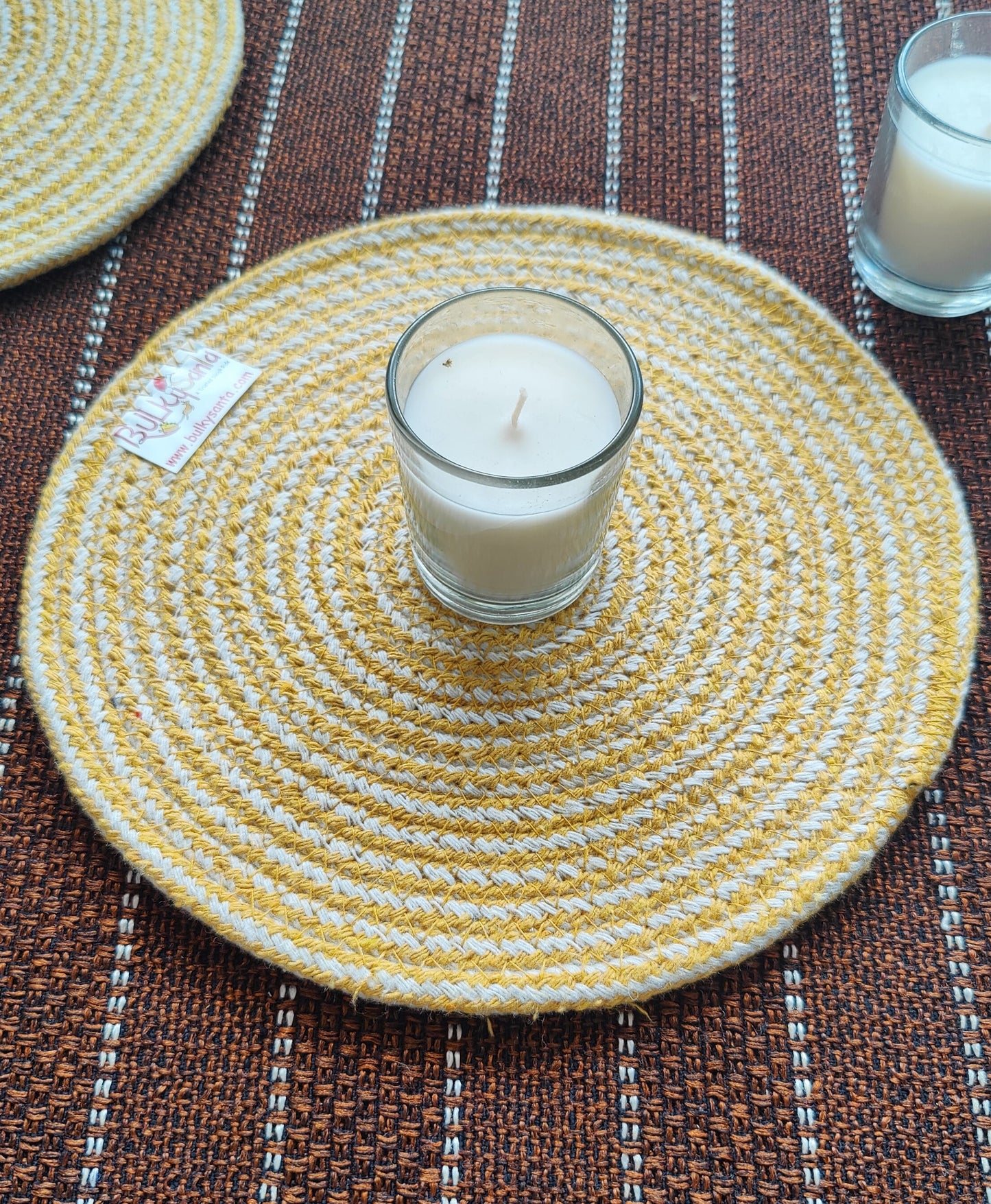 Yellow woven placemat with a glass of candle on a striped surface