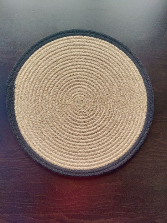 Black-beige spiral woven mat placed on a dark tabletop, shown as durable washable cotton placemats. Multi-Purpose Utility: Whether for daily meals or festive settings, these mats serve as trivets for dining table, bed side table cover mat, or heat resistant mats for dining table. Their design blends utility and decor effortlessly.