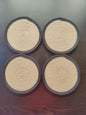 Four round woven coasters with beige center and dark gray border on a wooden surface.