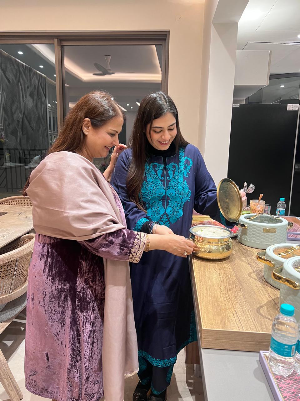 Two women in traditional attire preparing food in a kitchen.