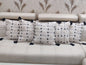 Decorative pillows with black tassels on a beige sofa against a patterned wallpaper background