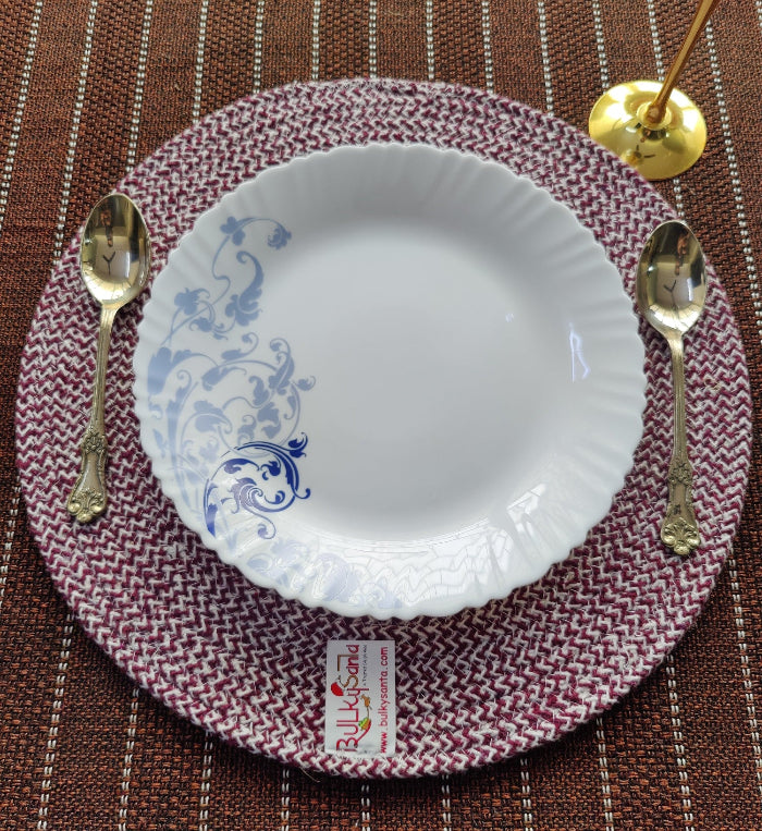White plate with blue floral design on a red woven placemat with silver spoons.