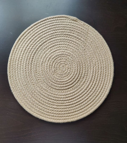 Beige braided round cotton placemat placed on a dark wooden table surface.